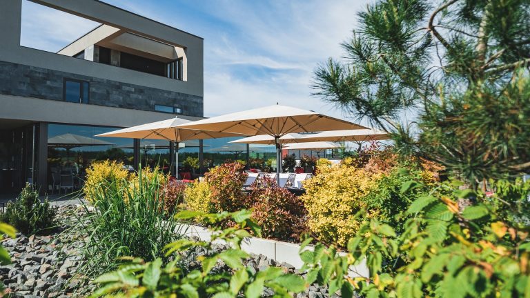 Die Terrasse des LAKESIDE Zwenkau bietet viel Grün, bequeme Sitzmöbel & große Sonnenschirme.