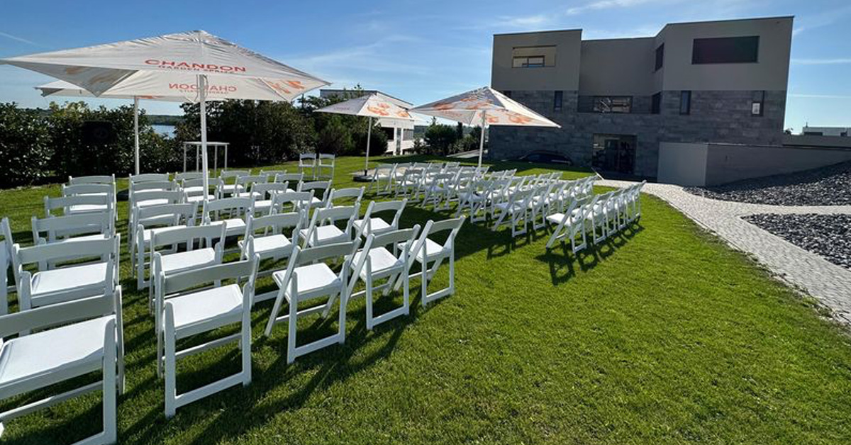 Blick über die Stuhlreihen weißer Stühle im Garten des LAKESIDE. Der Blick geht von links hinten über die Stühle Richtung Location im Hintergrund.