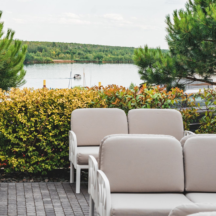 Ausschnitt der Terrasse des LAKESIDE mit hellen, modernen Sitzmöbeln und dem See im Hintergrund.