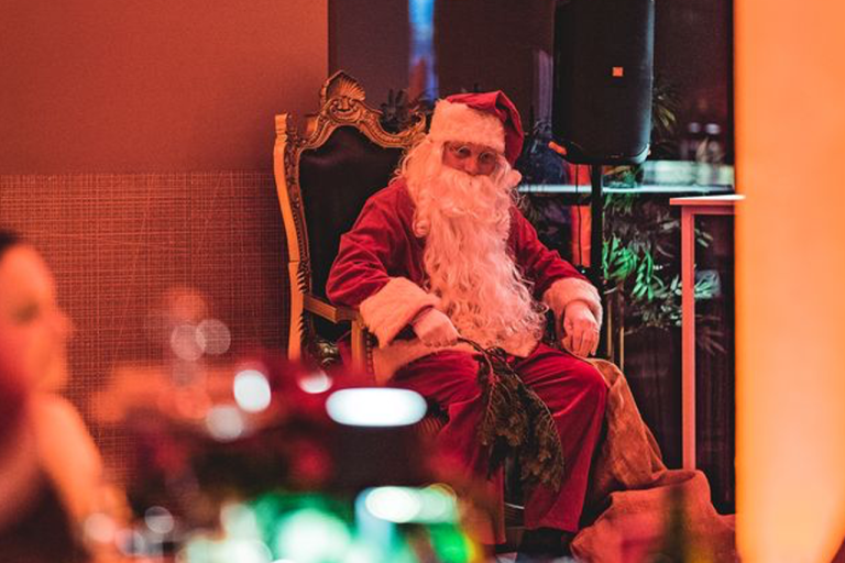 Ein Mann im Weihnachtsmannkostüm sitzt auf einem Thronsessel in der festlich beleuchteten Weihnachtsfeier Location