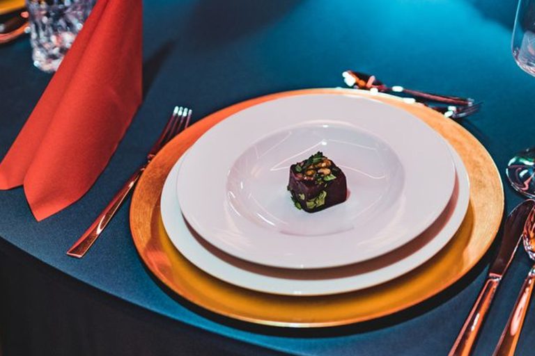 Tischsetting einer Weihnachtsfeier: goldener Platzteller auf petrolfarbener Tischdecke, darauf Hauptspeisen- und Suppenteller. Auf letzterem ist bereits die Einlage für den ersten Gang zu sehen, die später noch mit einer Suppe aufgefüllt wird