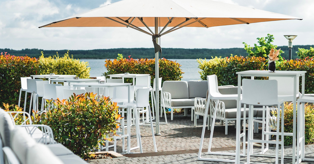 Setup für ein Firmen-Sommerfest im LAKESIDE: moderne weiße Möbel, hochwertige Schirme und ein toller Blick über den Zwenkauer See