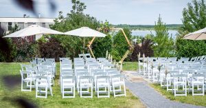 Blick über den Garten des LAKESIDE mit Trauungs-Setup aus Traubogen und weißen Stühlen in Richtung See.